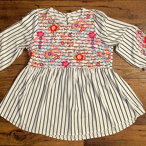 May include: White and black striped blouse with a floral embroidered design on the front and sleeves.