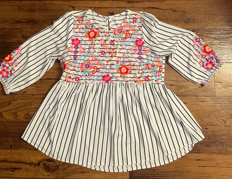 May include: White and black striped blouse with a floral embroidered design on the front and sleeves.