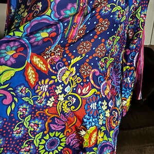 May include: A vibrant, long-sleeved tunic with a colorful floral and paisley pattern. The tunic features a button-down front and a mix of blue, purple, red, and yellow hues. The fabric appears to be lightweight, suitable for warmer weather.