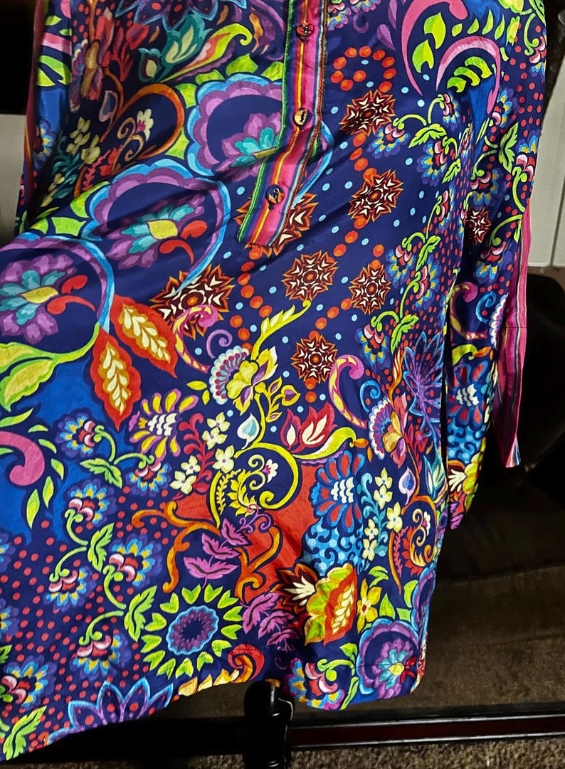 May include: A vibrant, long-sleeved tunic with a colorful floral and paisley pattern. The tunic features a button-down front and a mix of blue, purple, red, and yellow hues. The fabric appears to be lightweight, suitable for warmer weather.