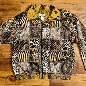 Puede incluir: Una chaqueta de color marrón, negro y dorado con estampado. La chaqueta tiene un diseño de patchwork con diferentes estampados de animales.