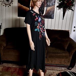 Puede incluir: Un vestido negro de manga corta con un dise&ntilde;o bordado colorido en el pecho. El bordado incluye fresas rojas, p&aacute;jaros azules y varios patrones florales en tonos rojos, azules, amarillos y verdes. El vestido tiene un dobladillo con volantes.