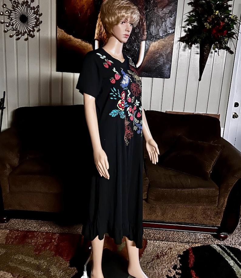 Puede incluir: Un vestido negro de manga corta con un dise&ntilde;o bordado colorido en el pecho. El bordado incluye fresas rojas, p&aacute;jaros azules y varios patrones florales en tonos rojos, azules, amarillos y verdes. El vestido tiene un dobladillo con volantes.