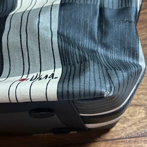 May include: A black and white striped tote bag with a black leather bottom and a black handle. The bag has a white label with the text "LLAMA" in red.