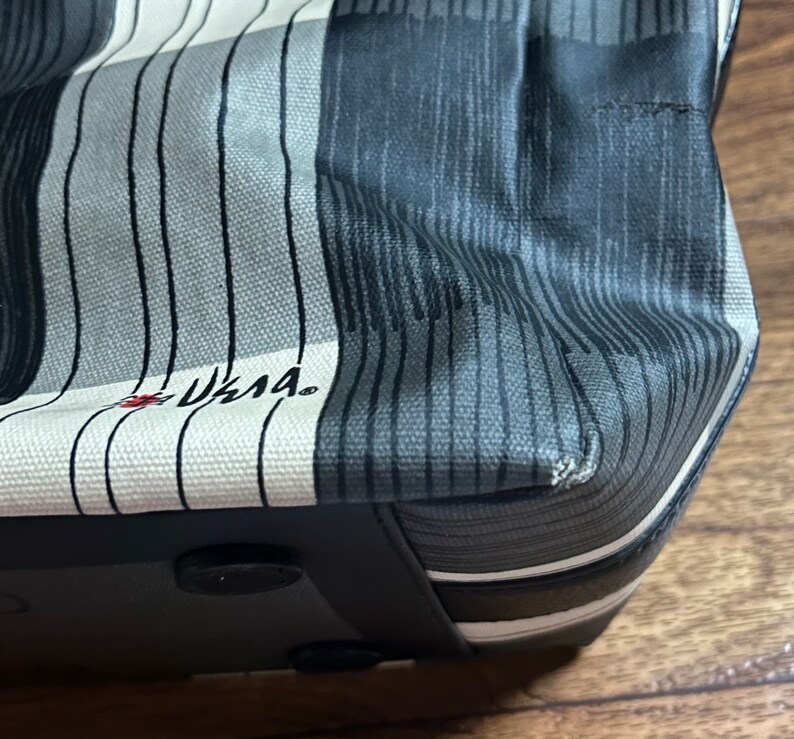 May include: A black and white striped tote bag with a black leather bottom and a black handle. The bag has a white label with the text "LLAMA" in red.