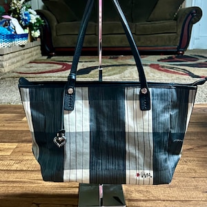 May include: A black and white plaid tote bag with black leather handles and a silver heart charm. The bag has the word "Vera" embroidered on the bottom in red.