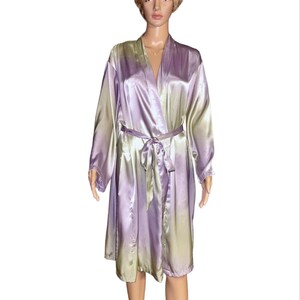 May include: A knee-length satin robe featuring a gradient color pattern that transitions between shades of light purple and pale green. The garment includes long sleeves, a shawl collar, and a matching fabric tie belt at the waist.