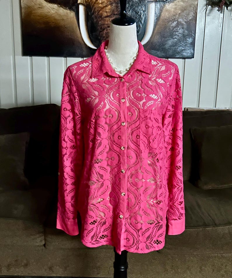 May include: A pink lace button-up shirt with long sleeves. The shirt has a delicate floral pattern and is semi-sheer.
