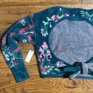 May include: A teal blue fuzzy knit sweater with a pink and green floral pattern. The sweater has a large open back with a tie at the bottom.