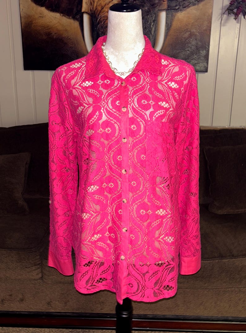 May include: A pink lace button-up shirt with long sleeves and a floral pattern.
