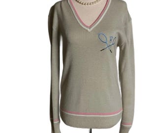 May include: Tan V-neck sweater with white and pink trim on the neckline, cuffs, and hem. Features an embroidered tennis racket and ball design in blue and black. A pearl necklace is draped around the neckline.