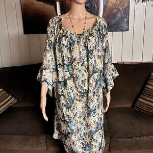 Puede incluir: Un vestido estampado en blanco y azul con cuello redondo y mangas 3/4. El vestido tiene un ribete con volantes en las mangas y un corte holgado y fluido.