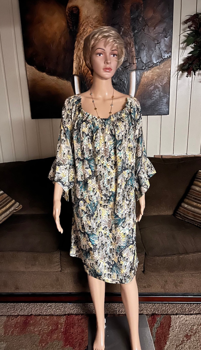 Puede incluir: Un vestido estampado en blanco y azul con cuello redondo y mangas 3/4. El vestido tiene un ribete con volantes en las mangas y un corte holgado y fluido.