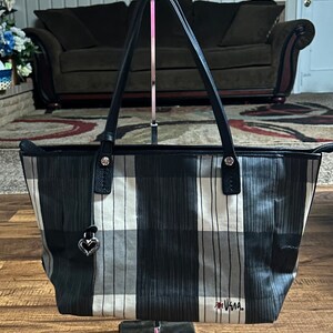 May include: A black and white plaid tote bag with black leather handles and a silver heart charm. The bag has the word "Vera" written on the bottom in red.