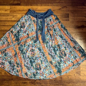 May include: A long, flowing skirt with a denim waistband and tie. The skirt features a colorful, intricate pattern in shades of teal, orange, and blue. The fabric has a soft, flowing drape, perfect for a casual, bohemian look.
