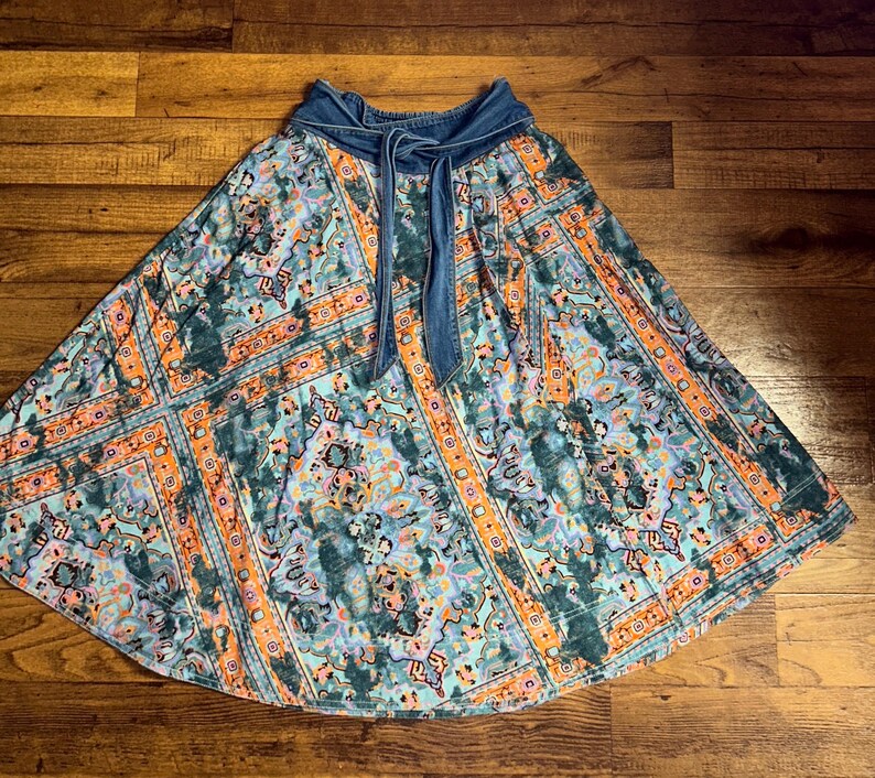May include: A long, flowing skirt with a denim waistband and tie. The skirt features a colorful, intricate pattern in shades of teal, orange, and blue. The fabric has a soft, flowing drape, perfect for a casual, bohemian look.