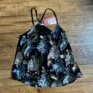 May include: A black sequined tank top with a floral pattern in shades of blue and gold. The top has a criss-cross strap design and a sheer overlay.
