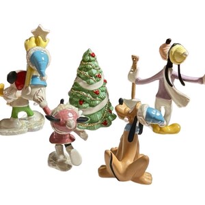 Może przedstawiać: Kolekcja ceramicznych figurek bożonarodzeniowych z postaciami Disneya. Figurki przedstawiają Myszka Miki, Myszka Minnie, Pluto i Goofy, wszyscy ubrani w zimowe stroje. W zestawie znajduje się r&oacute;wnież zielona choinka z czerwonymi ozdobami.