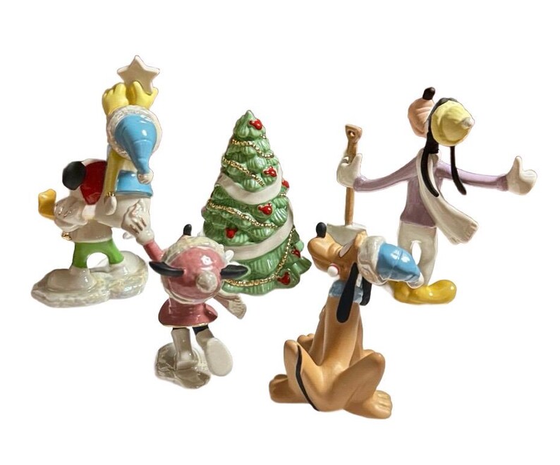 Może przedstawiać: Kolekcja ceramicznych figurek bożonarodzeniowych z postaciami Disneya. Figurki przedstawiają Myszka Miki, Myszka Minnie, Pluto i Goofy, wszyscy ubrani w zimowe stroje. W zestawie znajduje się r&oacute;wnież zielona choinka z czerwonymi ozdobami.