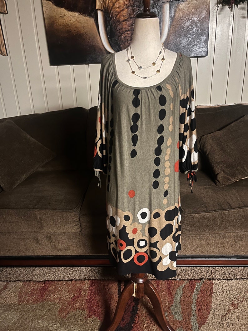 May include: A green, brown, black, white, and orange patterned dress with a scoop neck and 3/4 sleeves. The dress is on a mannequin and has a beaded necklace.