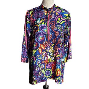 May include: A long-sleeved tunic with a vibrant floral and paisley pattern in shades of blue, purple, pink, yellow, and green. The tunic has a mandarin collar and a button-down placket. The sleeves are three-quarter length.