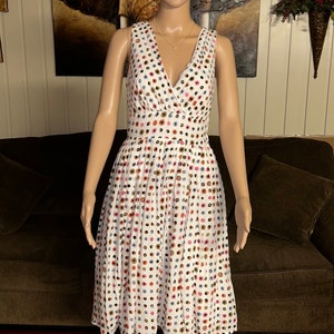 May include: White sleeveless dress with a V-neck and a flared skirt. The dress is adorned with a pattern of colorful polka dots in shades of pink, blue, brown, and gold. The dress is displayed on a mannequin.