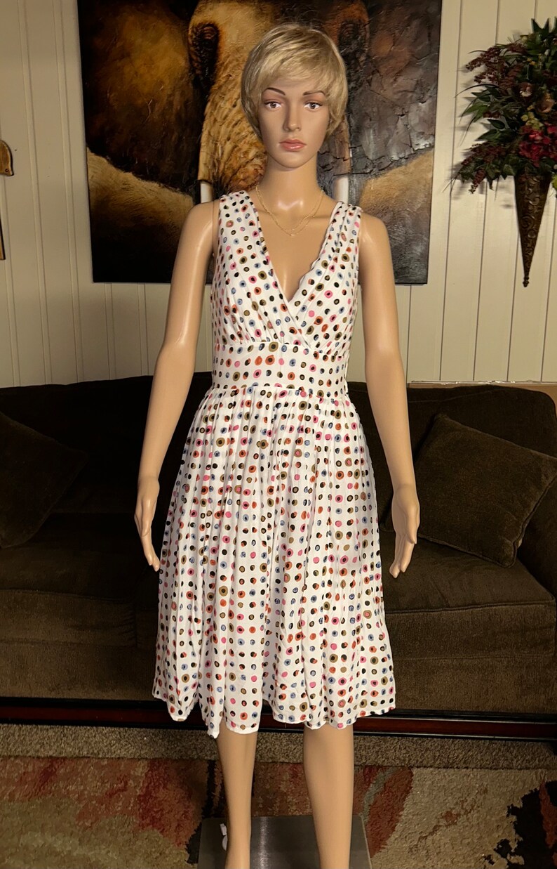 May include: White sleeveless dress with a V-neck and a flared skirt. The dress is adorned with a pattern of colorful polka dots in shades of pink, blue, brown, and gold. The dress is displayed on a mannequin.