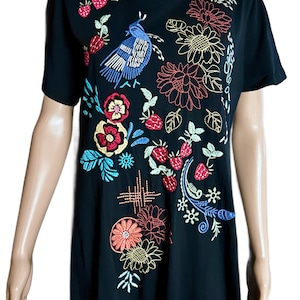 Puede incluir: Una camiseta negra de manga corta con bordados coloridos de un p&aacute;jaro azul, fresas rojas y varios patrones florales en tonos amarillo, naranja, rojo y azul. El dise&ntilde;o cubre la parte delantera de la prenda con costuras detalladas.