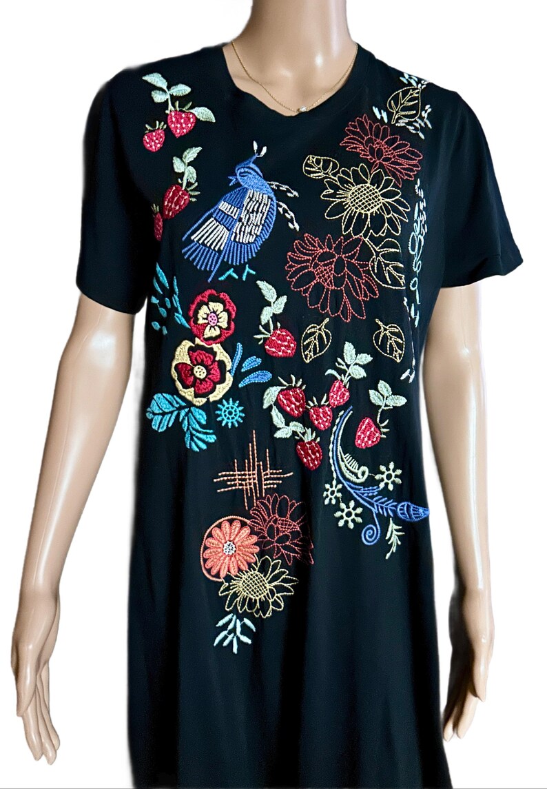 Puede incluir: Una camiseta negra de manga corta con bordados coloridos de un p&aacute;jaro azul, fresas rojas y varios patrones florales en tonos amarillo, naranja, rojo y azul. El dise&ntilde;o cubre la parte delantera de la prenda con costuras detalladas.