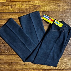 Może przedstawiać: Ciemnoniebieskie dżinsy Wrangler z denimu o prostym kroju nogawek. Dżinsy mają klasyczny styl z pięcioma kieszeniami i zapięciem na zamek błyskawiczny. Etykieta Wrangler jest dołączona. Dżinsy leżą na drewnianej powierzchni.