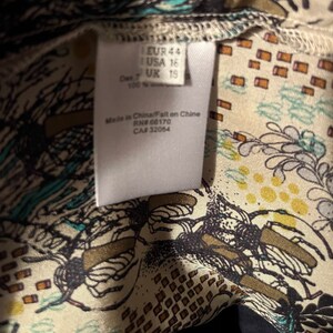 Puede incluir: Etiqueta blanca con texto negro que indica la talla EUR 44, USA 16, UK 15. La etiqueta tambi&eacute;n dice "Made in China/Fabriqu&eacute; en Chine" y "RN# 66170, CA# 32054". La etiqueta est&aacute; sobre una tela blanca con un patr&oacute;n floral negro y azul.