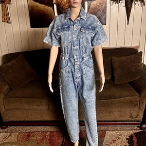 Peut inclure: Une combinaison en jean bleu clair &agrave; manches courtes et &agrave; fermeture boutonn&eacute;e. La combinaison a une coupe d&eacute;contract&eacute;e et une taille &agrave; cordon.