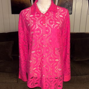 May include: A pink lace button-up shirt with long sleeves. The shirt has a floral pattern and is made of a delicate fabric.