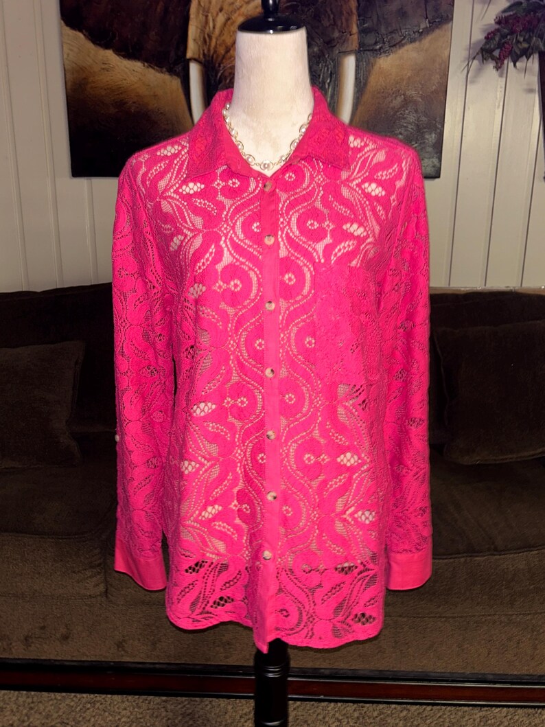 May include: A pink lace button-up shirt with long sleeves. The shirt has a floral pattern and is made of a delicate fabric.