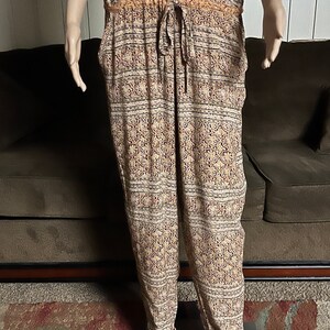 May include: A sleeveless jumpsuit with a beige background and a multi-colored floral pattern. The jumpsuit has a drawstring waist and a button closure at the front.