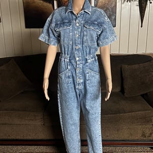 Peut inclure: Une combinaison en jean bleu clair &agrave; manches courtes et &agrave; fermeture boutonn&eacute;e. La combinaison a une coupe d&eacute;contract&eacute;e et un aspect l&eacute;g&egrave;rement d&eacute;lav&eacute;.