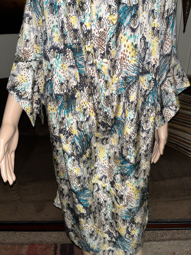 Puede incluir: Un vestido blanco, azul y marr&oacute;n con estampado y cierre de botones en la parte delantera. El vestido tiene un corte holgado y mangas cortas.