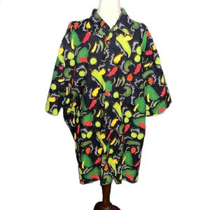 May include: A black short-sleeve button-down shirt featuring an all-over print of green, yellow, and red chili peppers and jalapeños. The fabric is covered in a repeating pattern of colorful peppers interspersed with the cursive white text jalapeños.