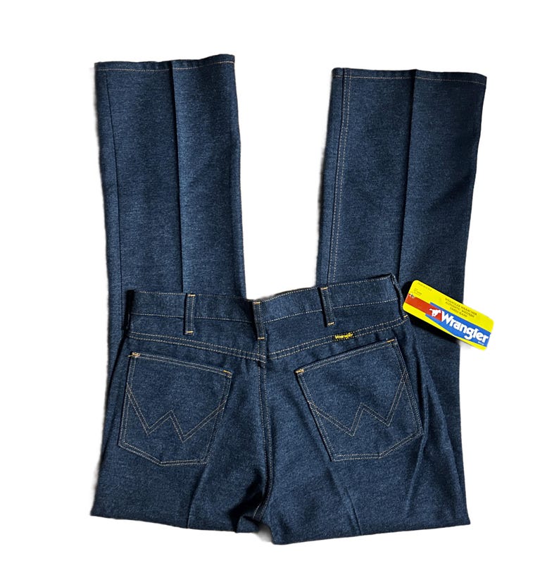 Może przedstawiać: Ciemnoniebieskie dżinsy Wrangler z klasycznym pięciokieszeniowym designem. Dżinsy mają prosty kr&oacute;j nogawek i logo Wrangler na tylnej kieszeni oraz ż&oacute;łto-czerwoną metkę. Dżinsy są nowe.
