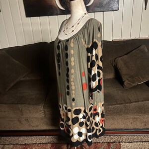 May include: A green, brown, black, and white patterned dress with a scoop neck and 3/4 sleeves. The dress is on a mannequin and has a floral pattern.
