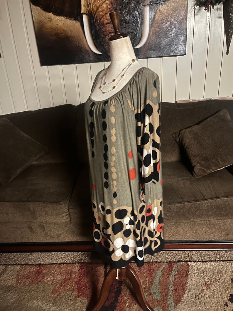 May include: A green, brown, black, and white patterned dress with a scoop neck and 3/4 sleeves. The dress is on a mannequin and has a floral pattern.