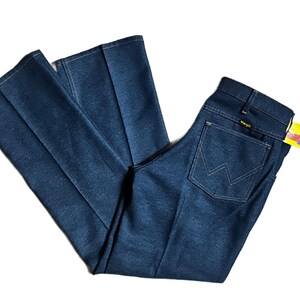 Może przedstawiać: Ciemnoniebieskie dżinsy Wrangler z denimu o klasycznym kroju. Dżinsy mają konstrukcję tylnej kieszeni z białymi przeszyciami oraz ż&oacute;łtą i białą metkę Wrangler. Dżinsy są złożone i ułożone płasko.