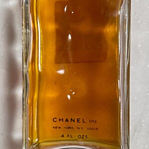 May include: A rectangular glass bottle filled with a golden liquid. The bottom of the bottle features the text "CHANEL Inc NEW YORK, N.Y. 10019" and "4 FL. OZS."