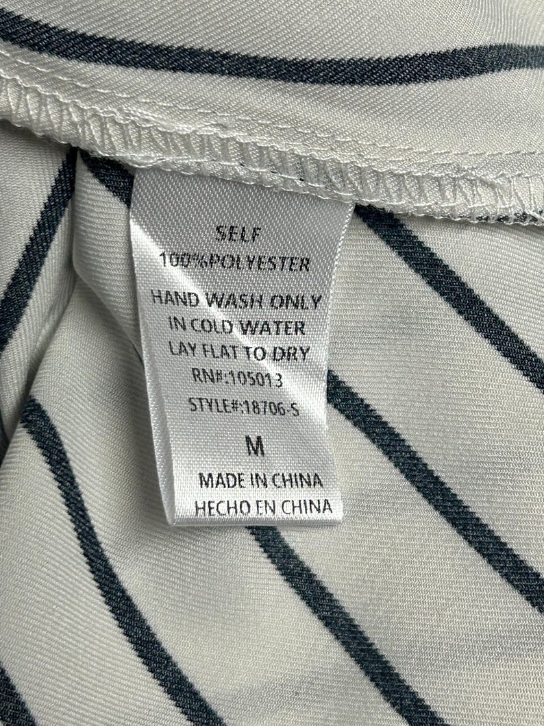 May include: White and black striped fabric with a white tag that says "SELF 100% POLYESTER HAND WASH ONLY IN COLD WATER LAY FLAT TO DRY RN#:105013 STYLE#:18706-5 M MADE IN CHINA HECHO EN CHINA"