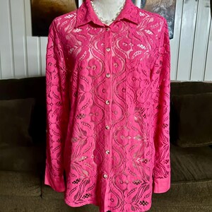 May include: A pink lace button-up shirt with long sleeves. The shirt has a delicate floral pattern and is semi-sheer.