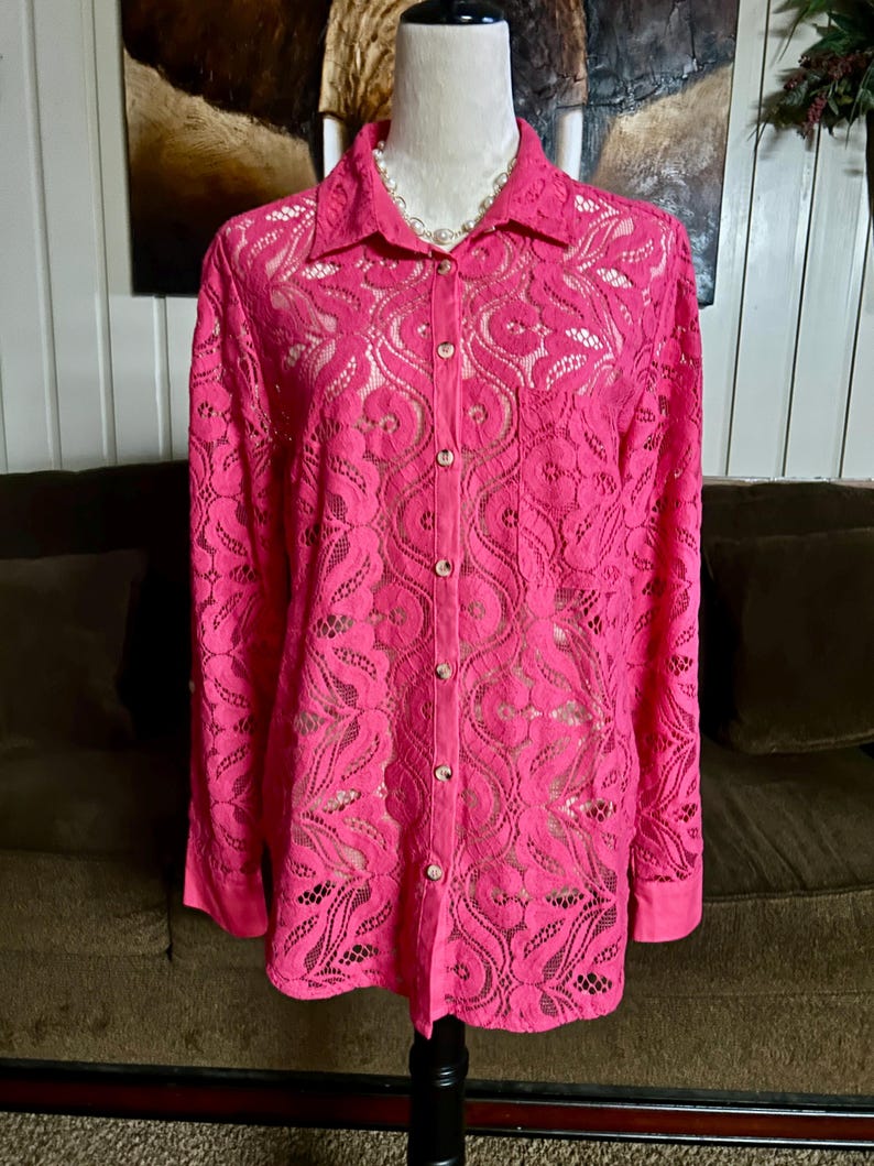 May include: A pink lace button-up shirt with long sleeves. The shirt has a delicate floral pattern and is semi-sheer.