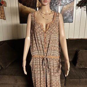 May include: A sleeveless, button-down jumpsuit with a brown, orange, and white patterned design. The jumpsuit has a drawstring waist and pockets.