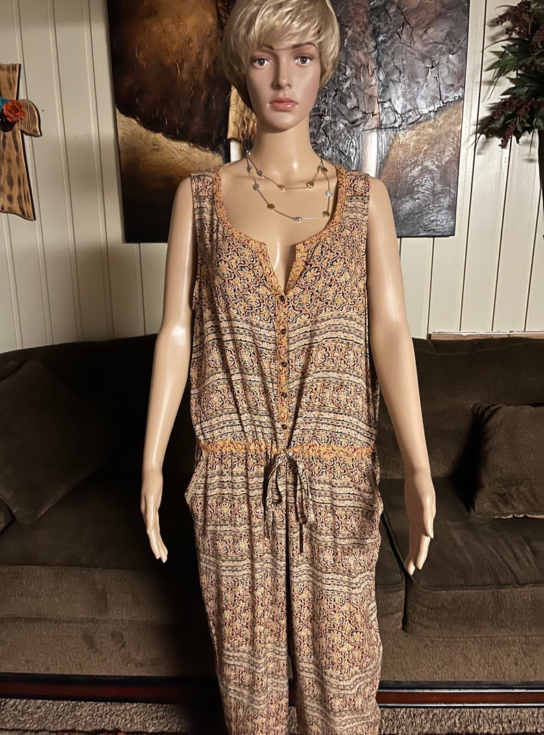 May include: A sleeveless, button-down jumpsuit with a brown, orange, and white patterned design. The jumpsuit has a drawstring waist and pockets.