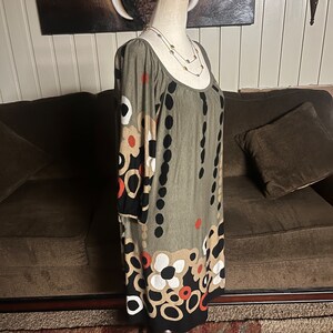 May include: A green, black, white, and orange patterned dress with 3/4 sleeves. The dress is on a white mannequin with a gold and silver necklace.