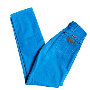 K&ouml;nnte beinhalten: Helle blaue Wrangler-Jeans. Die Jeans haben ein klassisches F&uuml;nf-Taschen-Design, einen braunen Lederaufn&auml;her auf der Ges&auml;&szlig;tasche und das Wrangler-Logo. Die Jeans sind auf wei&szlig;em Hintergrund gefaltet.